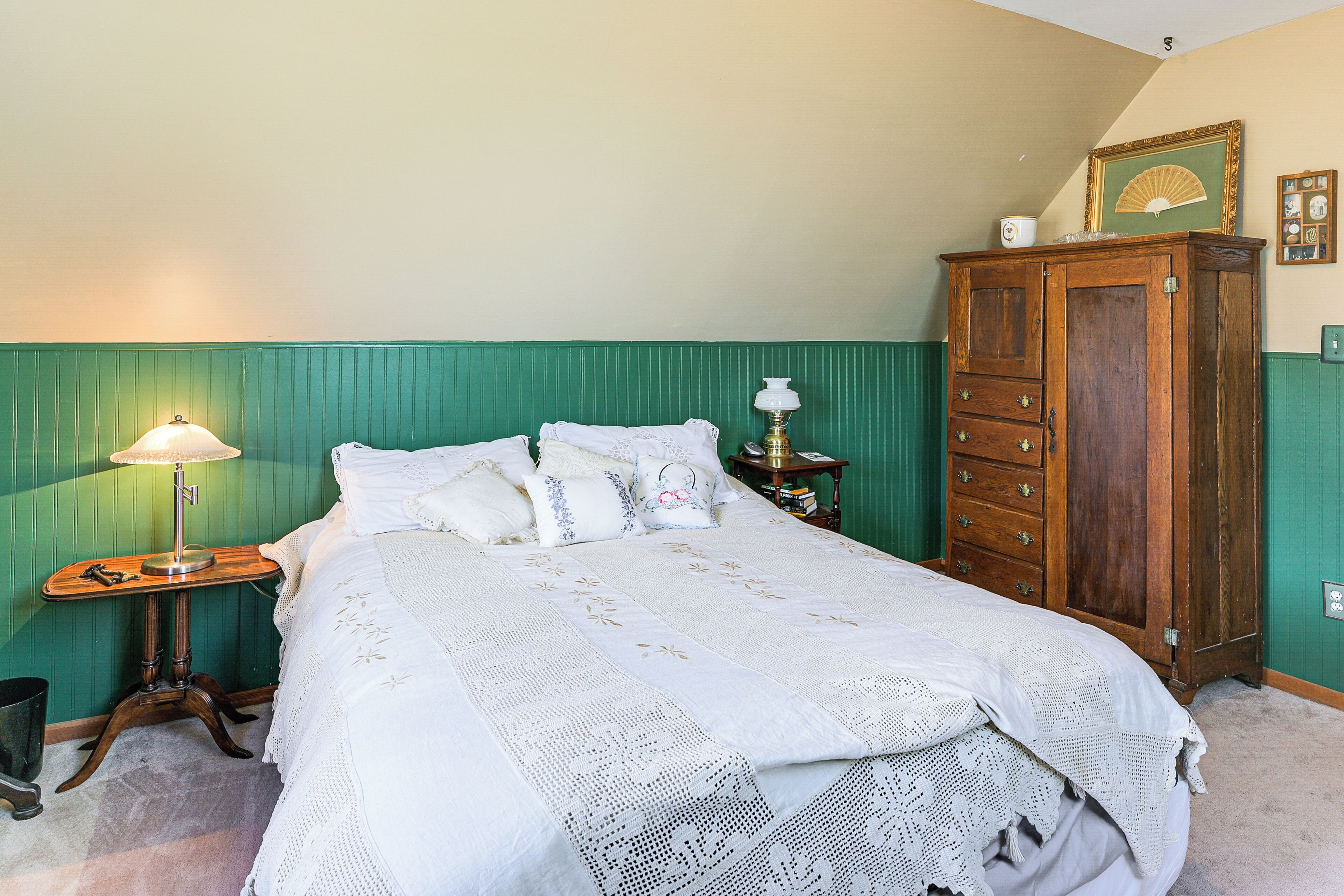 Ein Schlafzimmer mit einem Bett, einem Nachttisch, einer Holzkommode und einer grünen Wand.