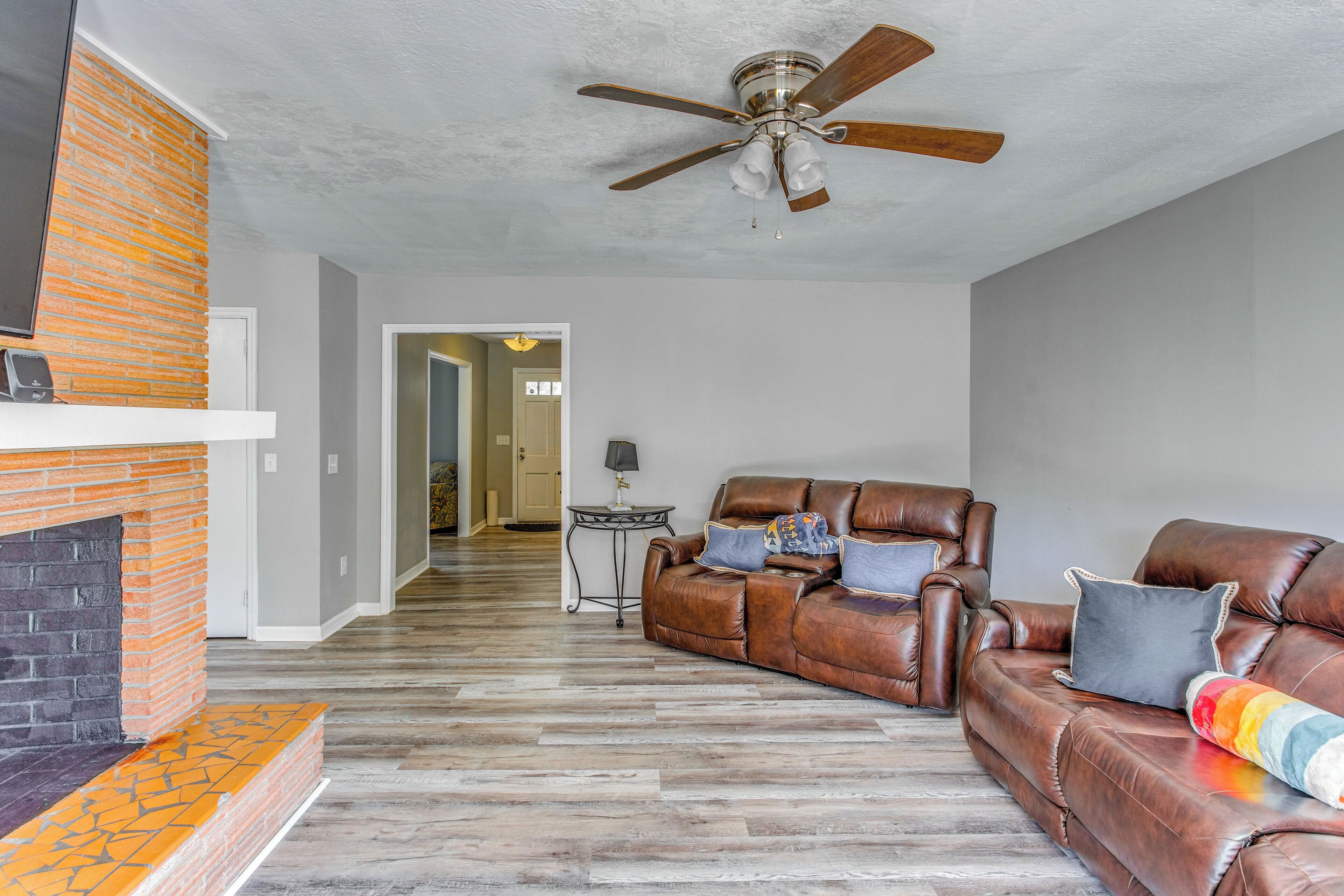 A living room with a brick fireplace, leather sofa, and a ceiling fan.