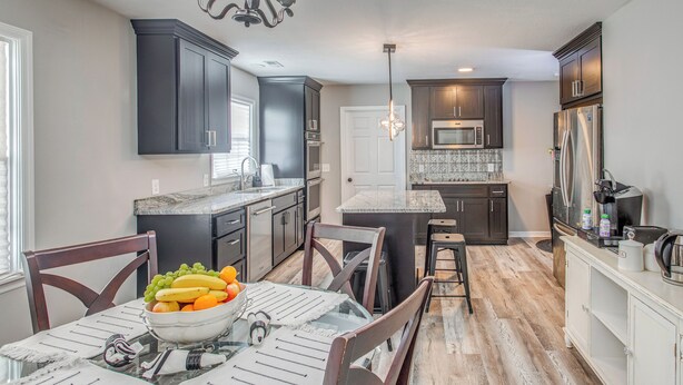 A modern kitchen with dark cabinets, a central island, and a dining area with a glass table. - 4 Mi to Loris Nature Park: Family Home w/ Yard (Loris)