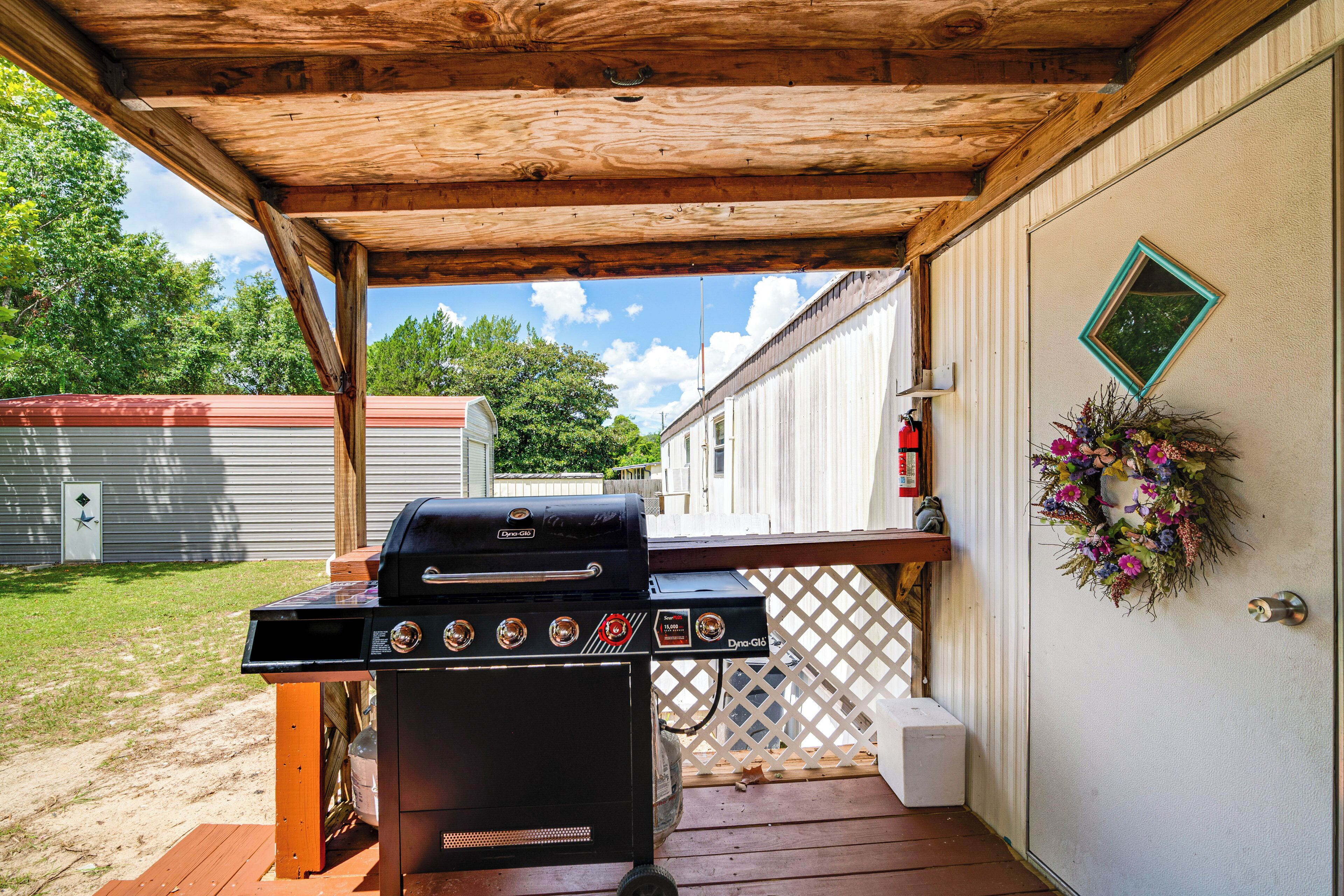 Un barbecue installé sous une pergola en bois, avec vue sur une maison et un jardin.