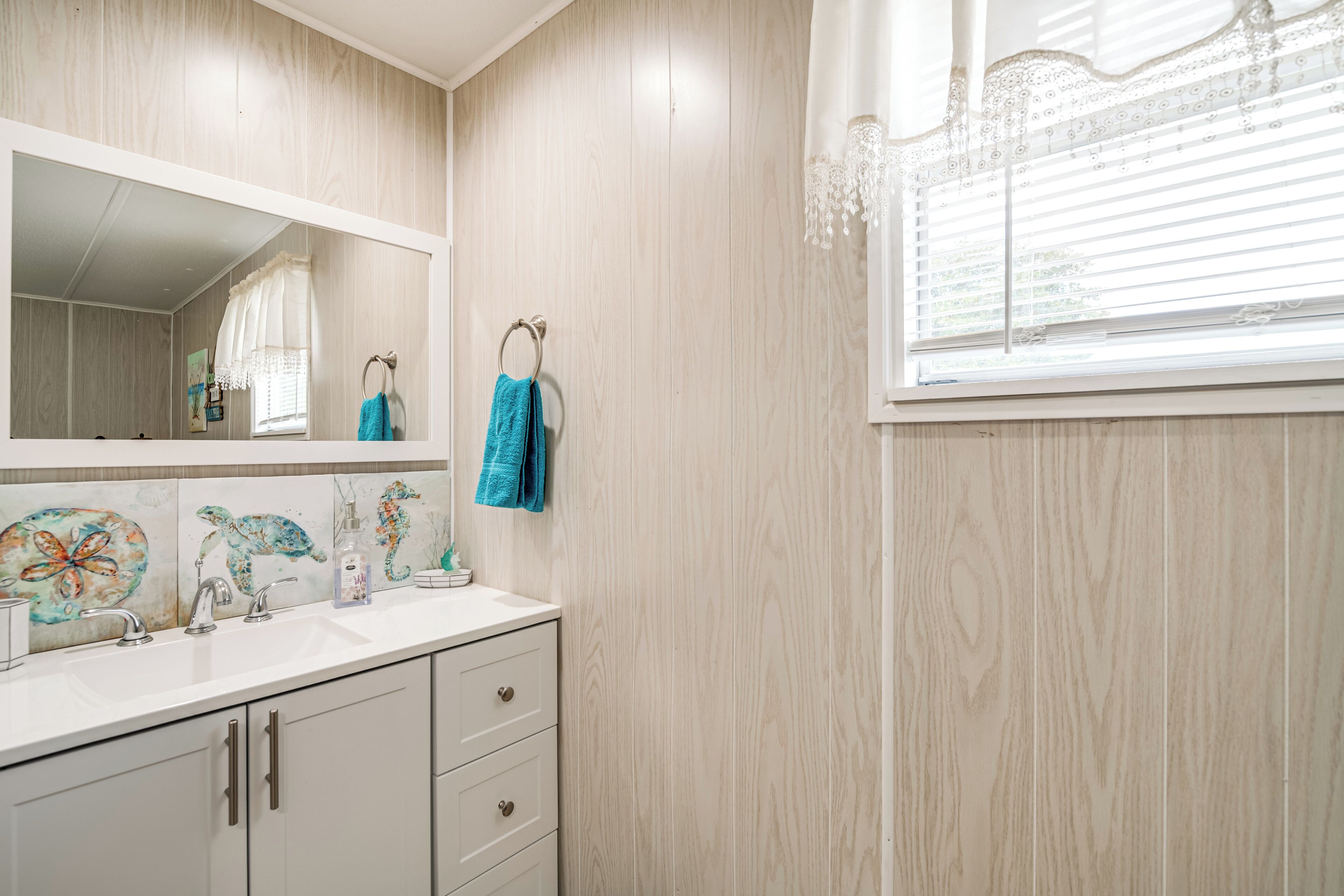 A bathroom with a wooden wall, a large mirror, a sink, and a window with a curtain.