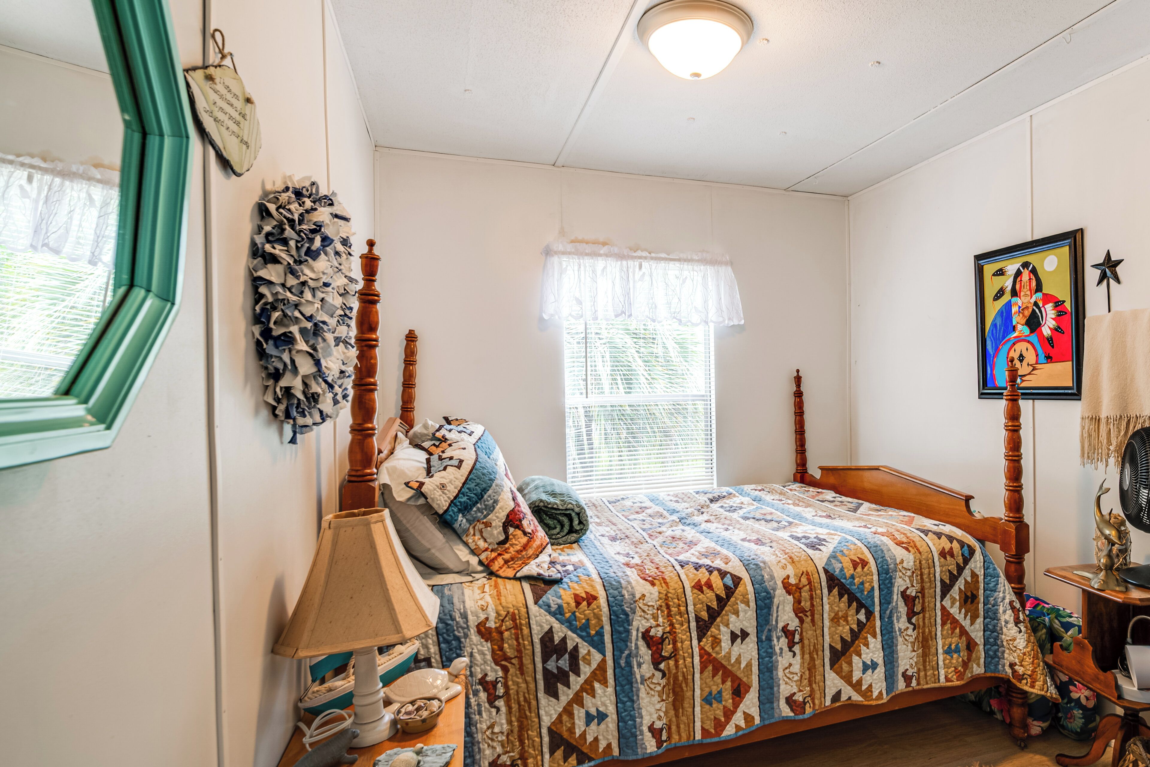Une chambre à coucher avec un lit en bois, une table de chevet avec une lampe, une fenêtre avec des stores et un tableau accroché au mur.