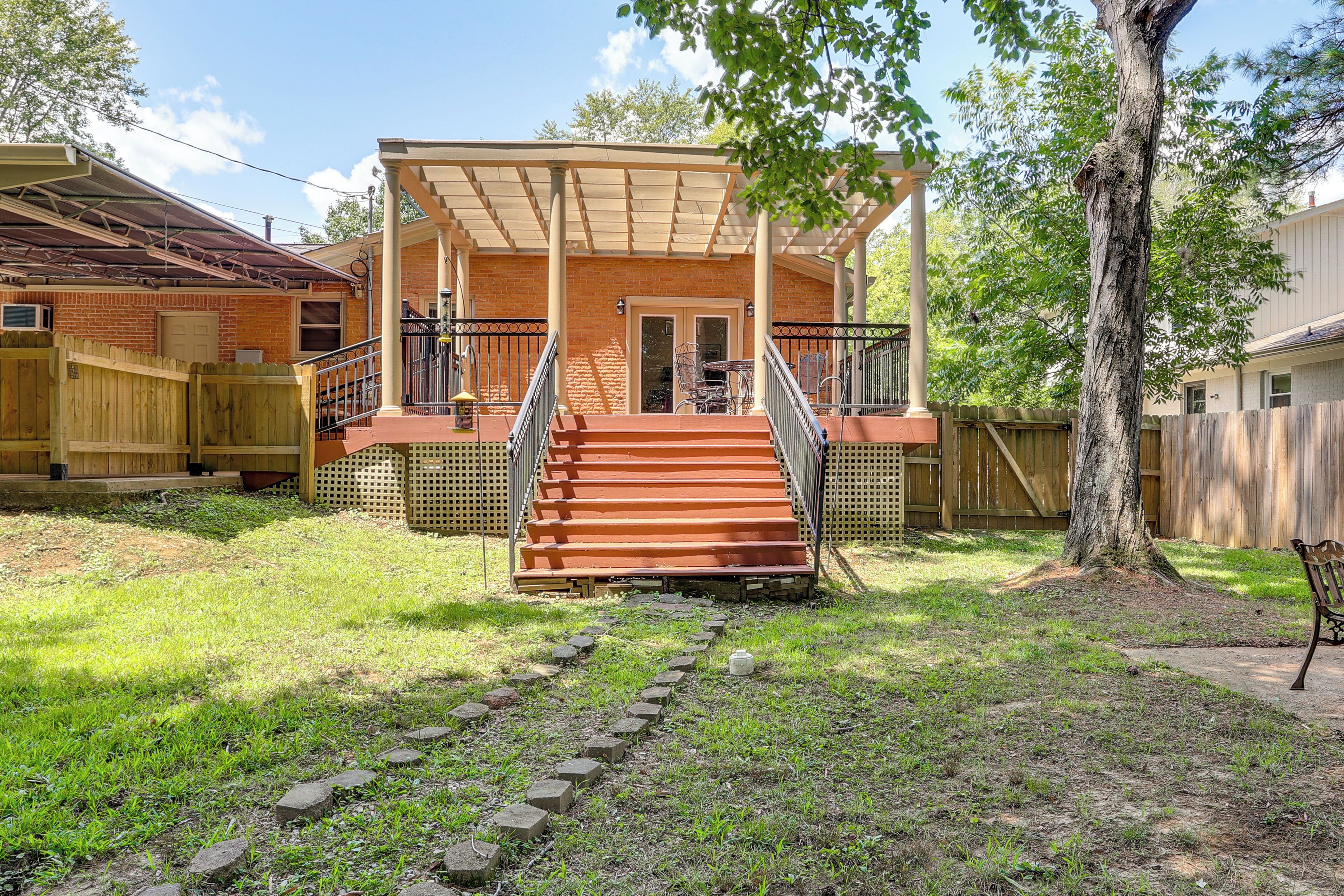 A covered porch with steps leading to a door, surrounded by a wooden fence and a tree.