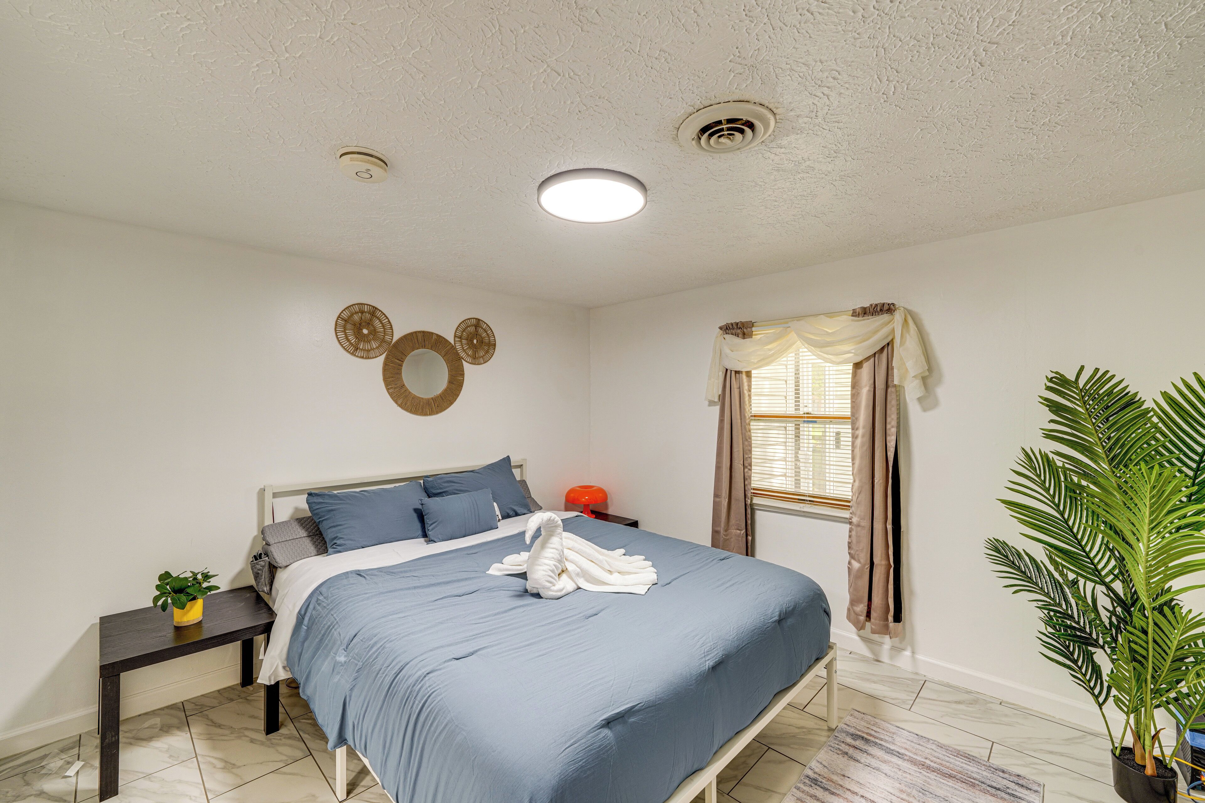 A bedroom with a bed, bedside tables, a wall clock, a window with curtains, and a potted plant.