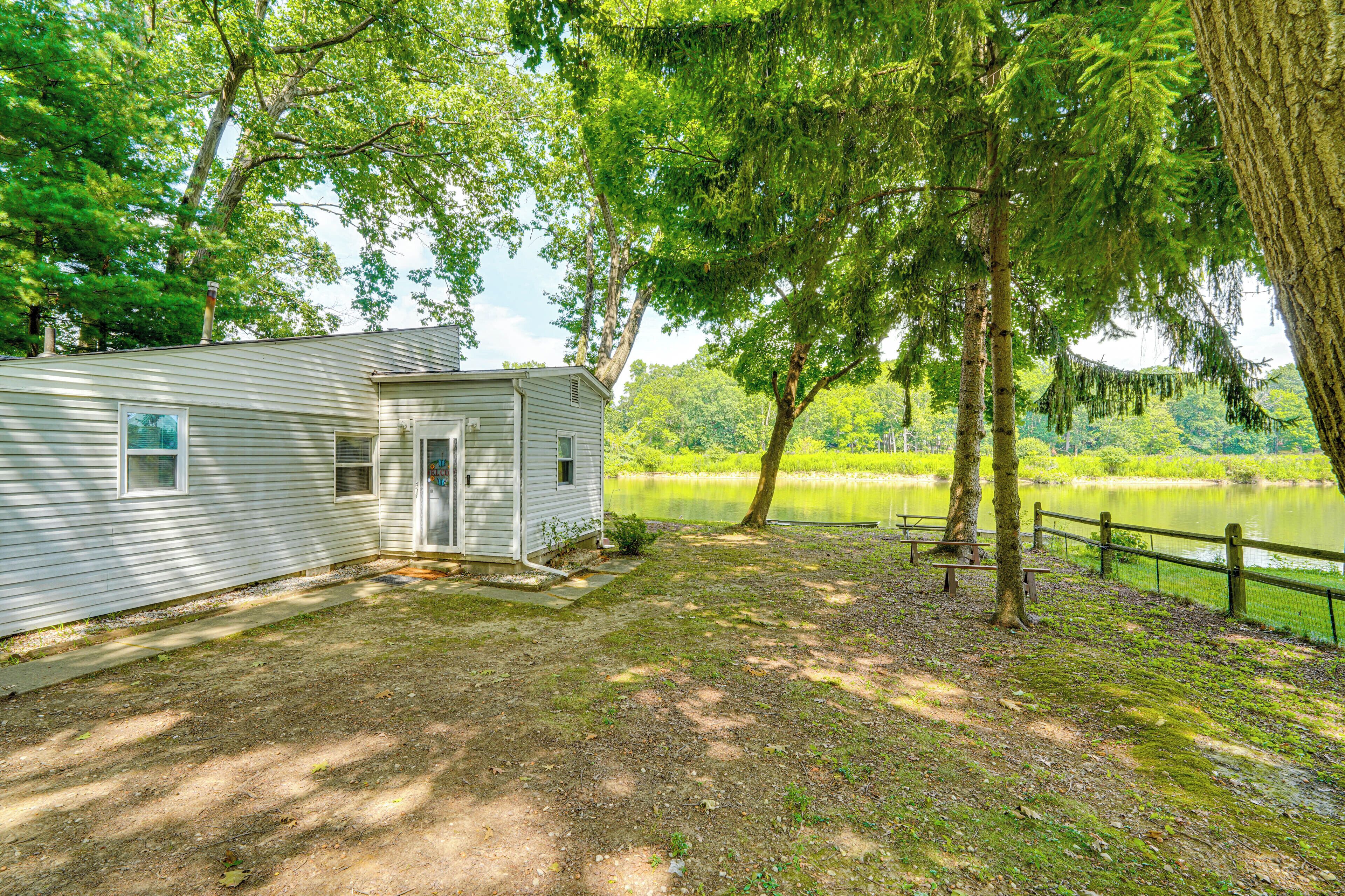 A small cabin with a porch, a pond, and a wooden fence.