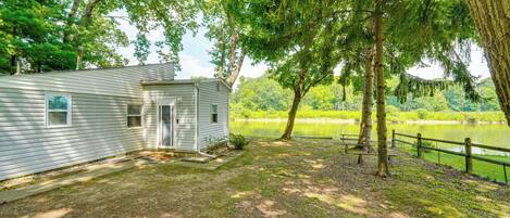 A small cabin with a porch, a pond, and a wooden fence.