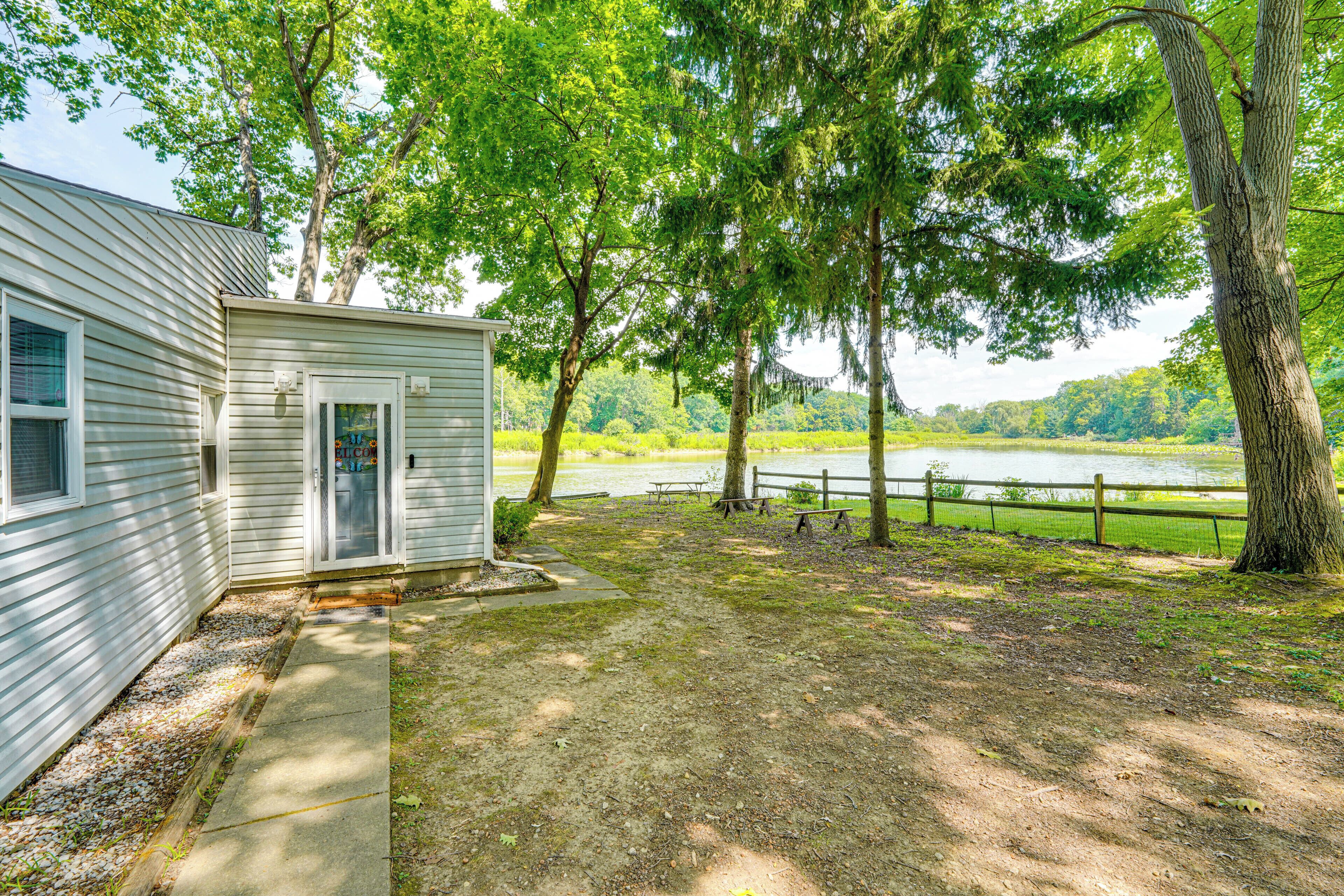 A cabin with a gravel path leading to a dock over a lake, surrounded by trees and a wooden fence.