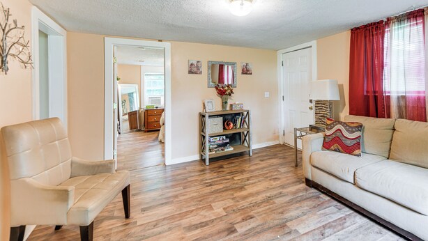 A living room with a beige sofa, a white armchair, and a wooden floor. There is a small table with a lamp and a decorative item. - 6 Mi to Museum of Aviation: Rural Kathleen Home (Kathleen)