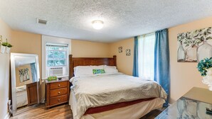 A bedroom with a wooden bed, a dresser, a mirror, a window with curtains, and a painting on the wall. - 6 Mi to Museum of Aviation: Rural Kathleen Home (Kathleen)
