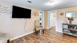 A living room with a flat-screen TV, a beige armchair, a bookshelf, and a wooden floor. - 6 Mi to Museum of Aviation: Rural Kathleen Home (Kathleen)