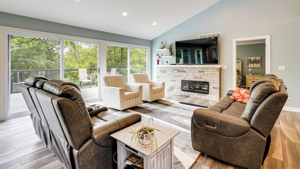 A spacious living room with a fireplace, leather sofas, and a large window overlooking a deck. - 4 Mi to Dtwn: Ohio River Valley Home w/ Deck! (Aurora)