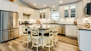 A modern kitchen with white cabinets, stainless steel appliances, a central island with bar stools, and a window with a 'Blessed' sign. - 4 Mi to Dtwn: Ohio River Valley Home w/ Deck! (Aurora)