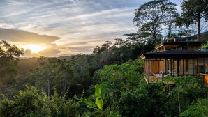 A modern house with a wooden deck and a hammock, surrounded by lush greenery and a mountainous backdrop. - w Stylish 1BR w Stunning Balcony Views (Cóbano)