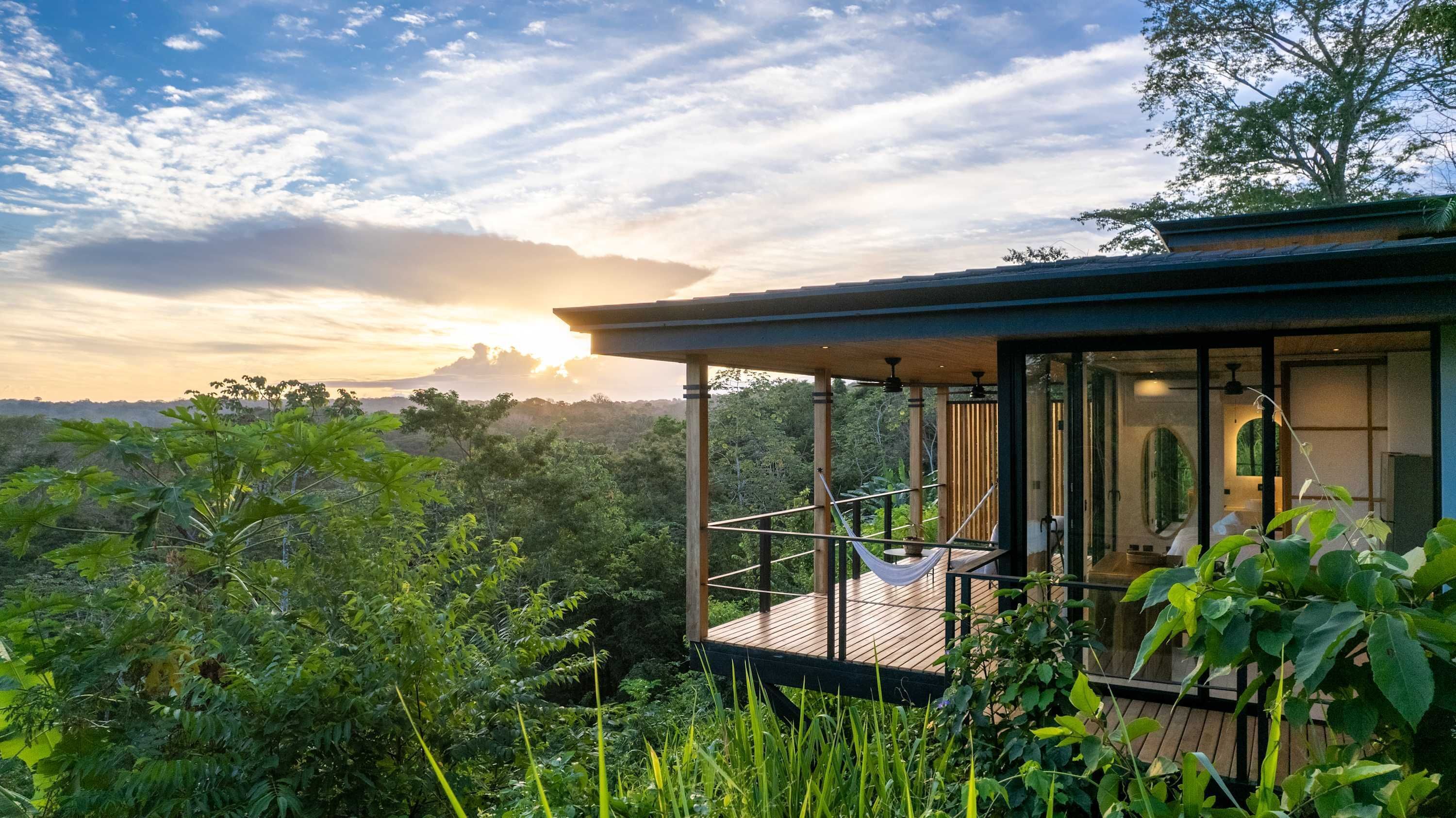 Una casa moderna con fachada de vidrio, terraza de madera y vistas al bosque circundante.