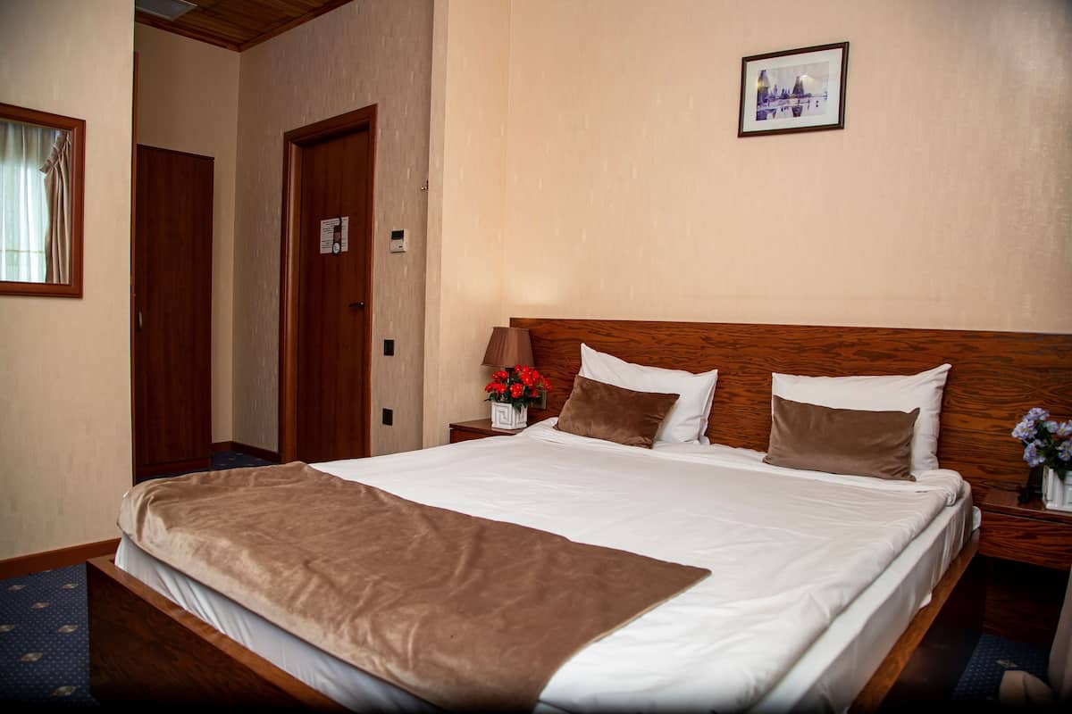 Una camera d'albergo con un letto grande, una testiera in legno e un comodino con un vaso di fiori.