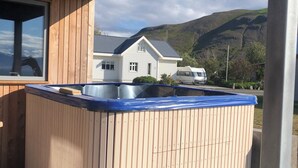 A hot tub under a wooden structure with a view of a house and mountains in the background.