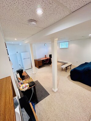 Une pièce comprenant un bureau, une chaise et un lit. Il y a une fenêtre avec des stores, une horloge au mur et un plafond avec un luminaire.