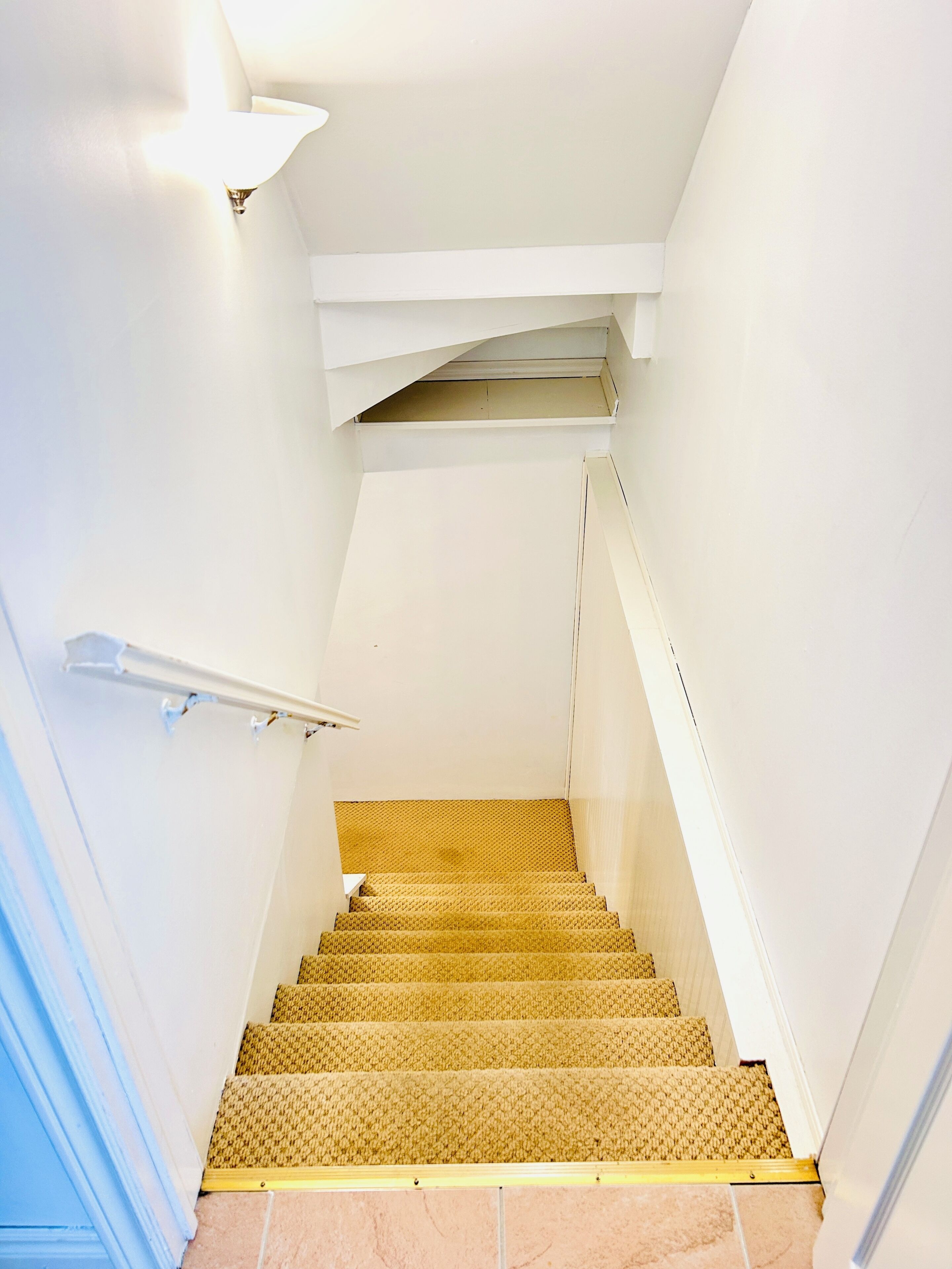 A staircase with a textured carpet, white walls, and a light fixture.