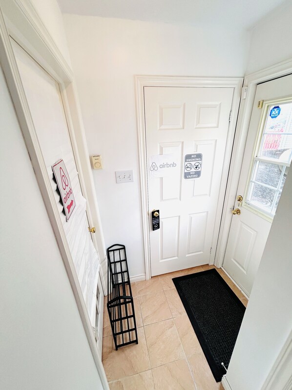 Un couloir avec une porte blanche, un paillasson noir à l’entrée et un petit porte-revues en métal noir.