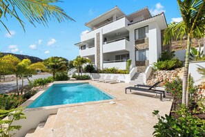 A modern two-story house with a swimming pool, outdoor seating, and a view of the surrounding landscape.