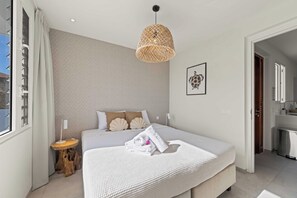 A modern bedroom with a large bed, a wooden nightstand, a woven light fixture, and a framed picture on the wall. - Caribbean Lounge — Elegant Island Apartment (Blue Bay Golf & Beach Resort)