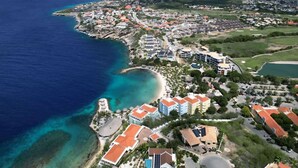 An aerial view of a coastal town with a beach, residential buildings, and a marina. - Caribbean Lounge — Elegant Island Apartment (Blue Bay Golf & Beach Resort)