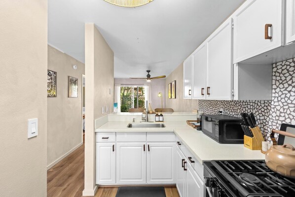 A kitchen with white cabinets, a black microwave, and a gas stove.
