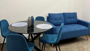 Un salón moderno con un sofá azul, una mesa redonda con sillas y dos cuadros abstractos en la pared.