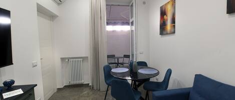 A compact living space with a dining table, blue chairs, a sofa, a TV, and a radiator.
