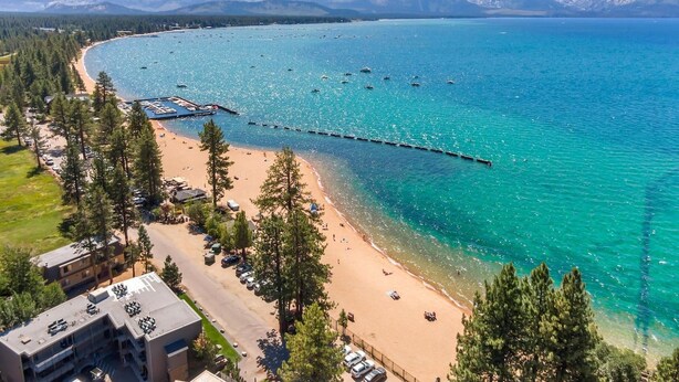 Una zona costera con playa, un muelle que se adentra en el agua y montañas al fondo.