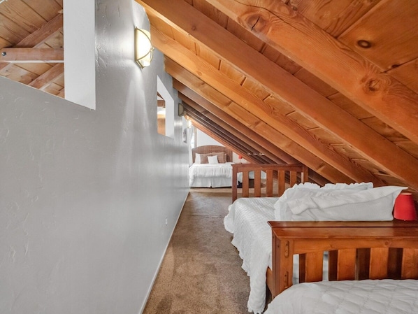 A room with a sloped ceiling, wooden beams, a bed with white bedding, and a red object on the bed. - Tahoe Cabin One Block from Lakeside Beach-Heavenly (South Lake Tahoe)