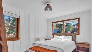 Un dormitorio con cama, mesita de noche, ventana y vistas al exterior.