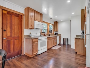 A kitchen with wooden cabinets, a white stove, and a stainless steel trash can. - Tahoe Cabin One Block from Lakeside Beach-Heavenly (South Lake Tahoe)