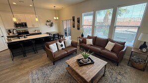 A modern living room with a brown leather sofa, a coffee table, and a dining area with a kitchen in the background. - Trailhead Hideaway ... a lovely 3-bedroom townhome in Washington, Utah (Washington)