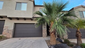 A two-story house with a stone facade, a dark garage door, and a palm tree in the front yard. - Trailhead Hideaway ... a lovely 3-bedroom townhome in Washington, Utah (Washington)
