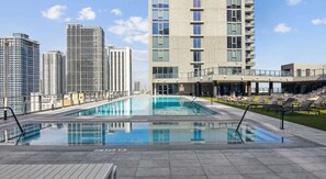 Una piscina en la azotea con vistas a rascacielos, sillas de descanso y una zona cubierta.