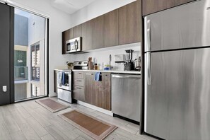 Una cocina moderna con electrodomésticos de acero inoxidable, armarios de madera y un ventanal corredero que da a un balcón.
