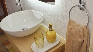 A bathroom with a white sink, a mirror, a towel rack, and a small tray with a glass and a bottle. - Traditional Cretan house, in the city center! (Chania)