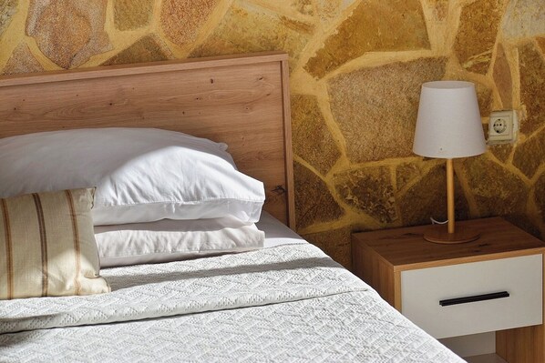 A bed with white linens, a wooden headboard, and a nightstand with a lamp and a drawer. - Traditional Cretan house, in the city center! (Chania)