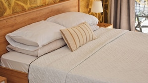 A neatly made bed with white linens and a beige pillow, set against a stone wall backdrop. - Traditional Cretan house, in the city center! (Chania)