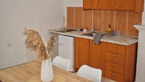 A compact kitchen with wooden cabinets, a white refrigerator, and a marble countertop. - Traditional Cretan house, in the city center! (Chania)