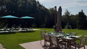 Un patio al aire libre con una mesa lista para comer, rodeado de sillas y dos sombrillas que brindan sombra.