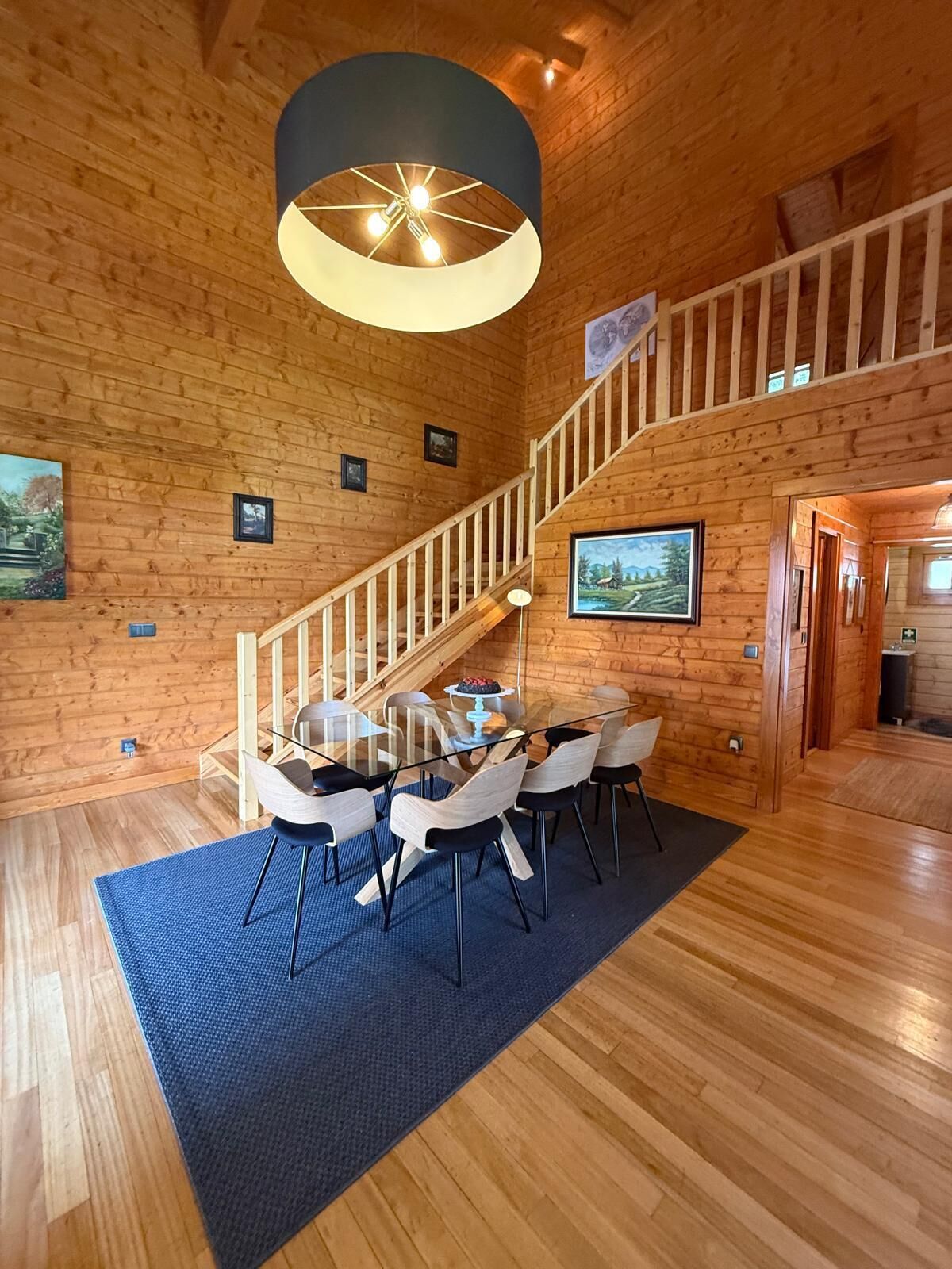 Un interior de madera con una escalera, comedor y cuadros en las paredes.