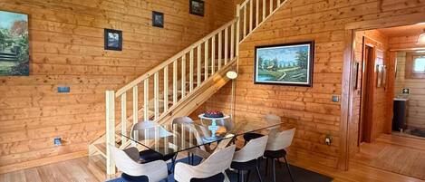 Un interior de madera con una escalera, comedor y cuadros en las paredes.