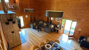 A spacious wooden cabin interior with a large L-shaped sofa, a dining area with chairs, and a stone fireplace. - Gerês Nature House (Terras de Bouro)