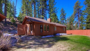 Une cabane en bois avec un toit en pente, une véranda à l’avant et une cour clôturée.