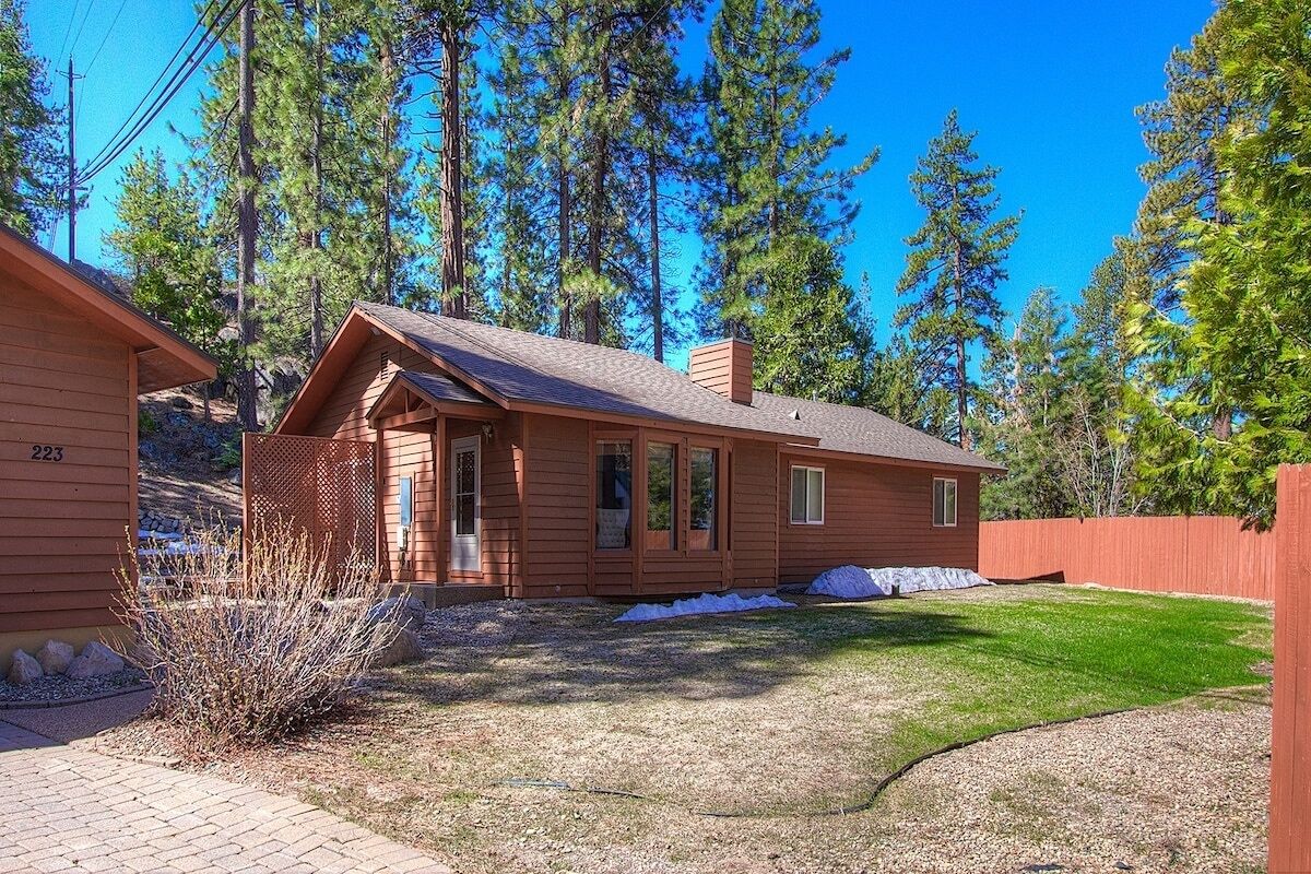 A single-story wooden cabin with a sloped roof, a front porch, and a fenced yard.