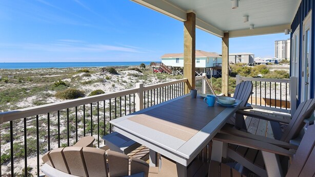 A balcony with a table and chairs overlooking a beach and ocean. - Cole's Houses 4159-4 4 Bedroom Home (Gulf Shores)