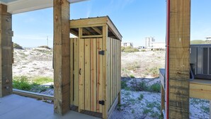 A wooden structure with a door, possibly a storage shed or utility room, in a sandy outdoor area with a clear sky. - Cole's Houses 4159-4 4 Bedroom Home (Gulf Shores)