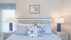 A bedroom with a bed, two nightstands, a headboard, a window with blinds, and a framed picture on the wall. - Cole's Houses 4159-4 4 Bedroom Home (Gulf Shores)